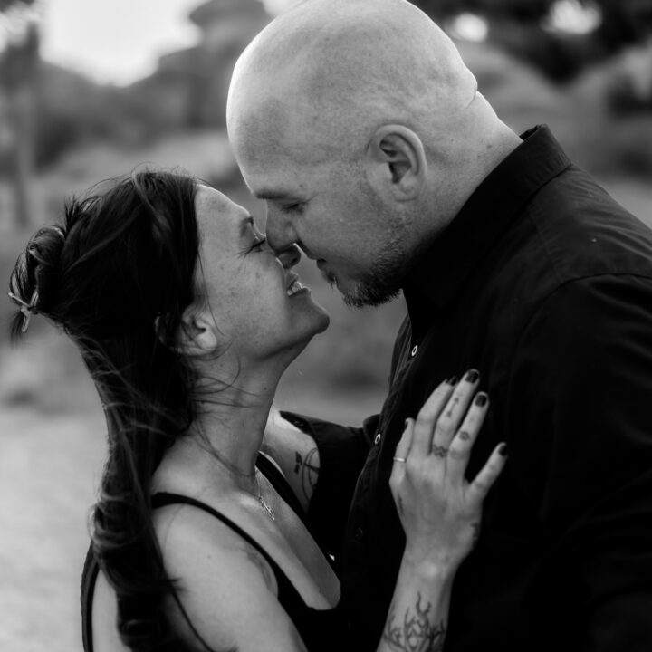 A black and white image of a couple sharing a joyful, intimate moment with their noses touching and eyes closed. They hold each other lovingly, smiling and lost in the connection.